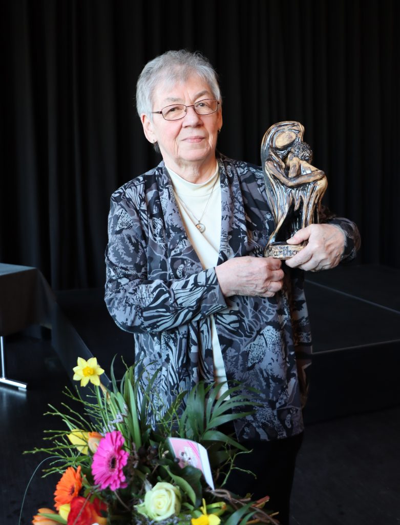Helga Nickich mit der Martha-Plastik vor Blumen
