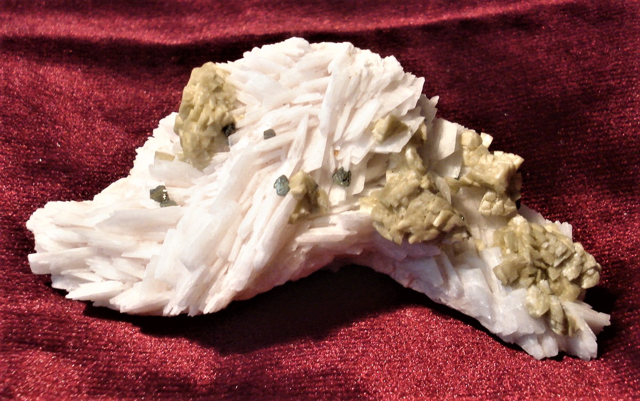 Zu sehen ist ein weiß-gelbliches Mineralgestein auf einer weinroten Samtunterlage.