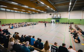 Es ist eine totale Ansicht der Drei-Feld-Sporthalle zu sehen. Schüler am Rand ringherum. Hoyerswerdas Oberbürgermeister Torsten Ruban-Zeh steht in der Mitte der Halle mit einem Mikrofon in der Hand und hält eine Rede.