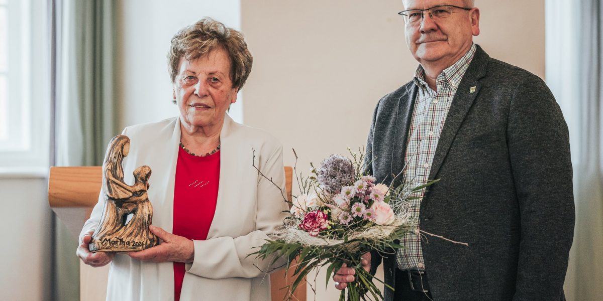 Dr. Gitta Kaltschmidt steht neben Hoyerswerdas Oberbürgermeister Torsten Ruban-Zeh im Großen Saal des Schlosses Hoyerswerda. Beide lächeln in die Kamera. Frau Dr. Kaltschmidt hält die Martga-Auszeichnung in der Hand. Herr Ruban-Zeh einen Blumenstrauß.