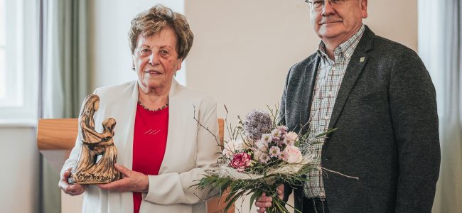 Dr. Gitta Kaltschmidt steht neben Hoyerswerdas Oberbürgermeister Torsten Ruban-Zeh im Großen Saal des Schlosses Hoyerswerda. Beide lächeln in die Kamera. Frau Dr. Kaltschmidt hält die Martga-Auszeichnung in der Hand. Herr Ruban-Zeh einen Blumenstrauß.