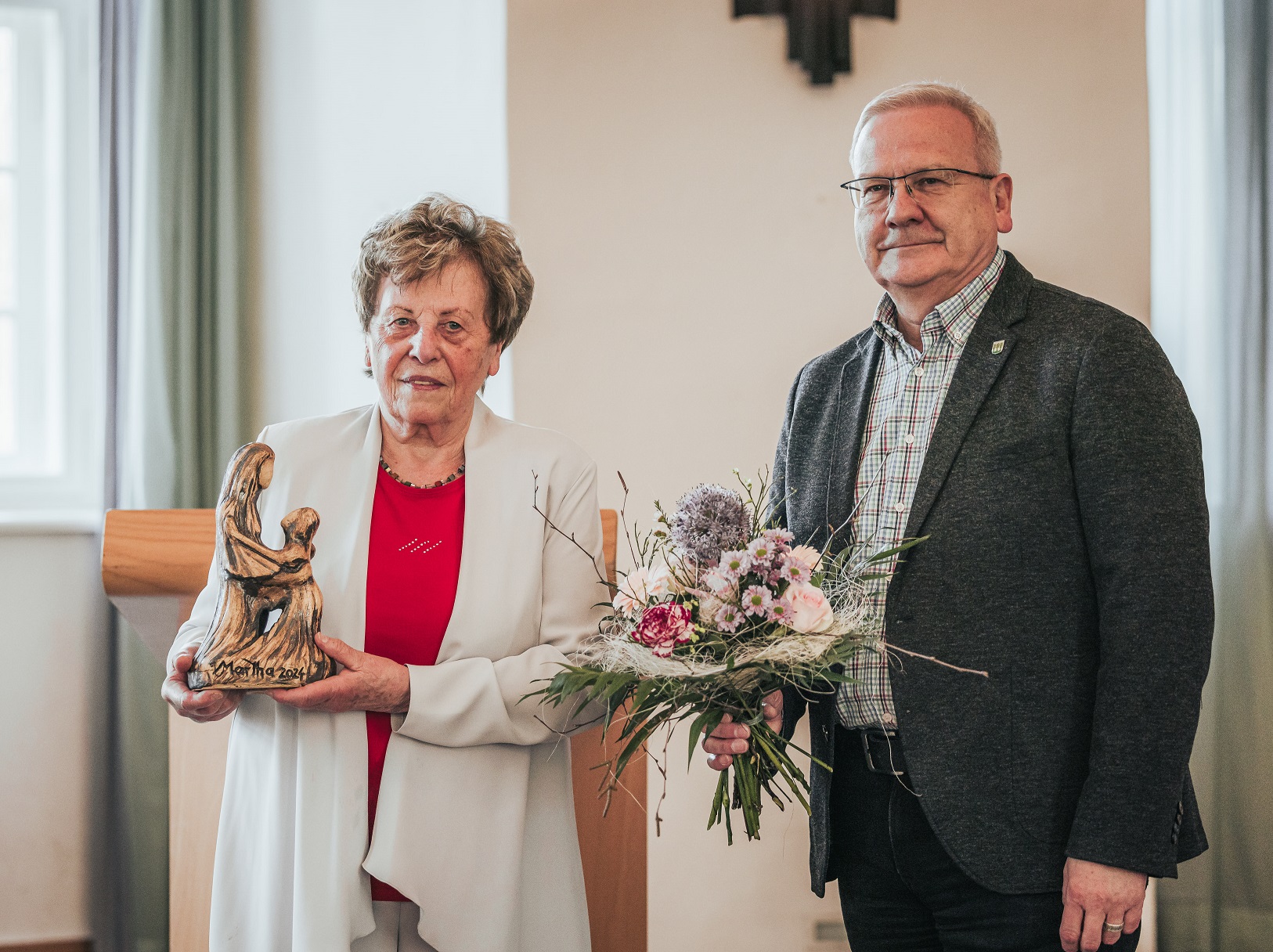 Dr. Gitta Kaltschmidt steht neben Hoyerswerdas Oberbürgermeister Torsten Ruban-Zeh im Großen Saal des Schlosses Hoyerswerda. Beide lächeln in die Kamera. Frau Dr. Kaltschmidt hält die Martga-Auszeichnung in der Hand. Herr Ruban-Zeh einen Blumenstrauß.