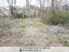 Es ist ein Teil der Hundefreilauffläche zu sehen und der zerstörte Zaun, der teilweise auf der Wiese liegt.