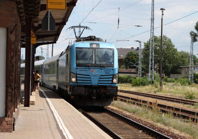 Der polnische Intercity-Zug mit der Lokomotive in hellblauer Lackierung hält am Bahnsteig. Zwei Personen filmen und fotografieren die Ankunft aus nächster Nähe.
