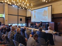 Zwei Mädchen und eine Frau spielen Geige und Cello auf der Bühne der Lausitzhalle Hoyerswerda. Hinter ihnen ist eine große Leinwand mit historischen Bildern zu sehen. Das Publikum verfolgt den Auftritt aufmerksam.