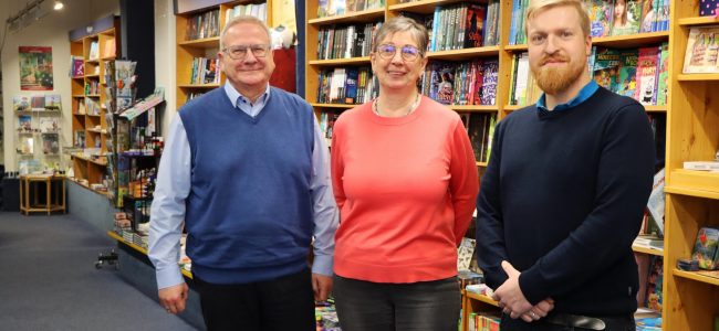 Drei Personen stehen in einer Buchhandlung vor gut gefüllten Bücherregalen. Links steht der Oberbürgermeister der Stadt Hoyerswerda, in der Mitte die Inhaberin des Buch und Musikhauses Sygusch, rechts der Wirtschaftsförderer der Stadt. Alle blicken in die Kamera.