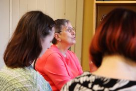 In einer Buchhandlung sitzt Elisabeth Sygusch am Tisch und spricht. Im Vordergrund sind weitere Personen unscharf zu sehen, die ihr zuhören.