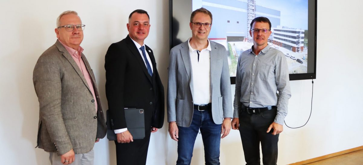 Vier Männer stehen nebeneinander in einem hellen Raum vor einem großen Bildschirm. Von links nach rechts: Torsten Ruban-Zeh (Oberbürgermeister Stadt Hoyerswerda), Udo Witschas (Landrat Landkreis Bautzen), Prof. Dr.-Ing. Günther Prokop (TU Dresden, Sprecher des Smart Mobility Lab) und Tobias Zschieschick (Koordinator Smart Mobility Lab). Auf dem Bildschirm ist eine Visualisierung eines modernen Gebäudekomplexes zu sehen.