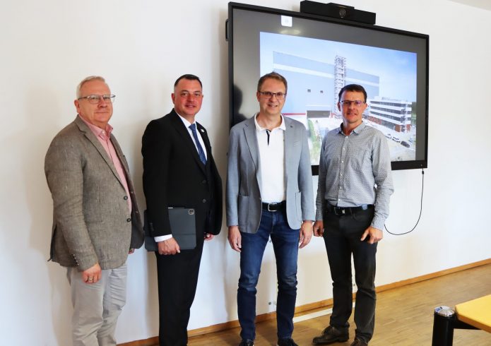 Vier Männer stehen nebeneinander in einem hellen Raum vor einem großen Bildschirm. Von links nach rechts: Torsten Ruban-Zeh (Oberbürgermeister Stadt Hoyerswerda), Udo Witschas (Landrat Landkreis Bautzen), Prof. Dr.-Ing. Günther Prokop (TU Dresden, Sprecher des Smart Mobility Lab) und Tobias Zschieschick (Koordinator Smart Mobility Lab). Auf dem Bildschirm ist eine Visualisierung eines modernen Gebäudekomplexes zu sehen.
