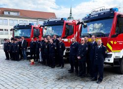 Gruppenfoto von Feuerwehrkameradinnen und Feuerwehrkameraden vor drei neuen Löschgruppenfahrzeugen auf dem Marktplatz in Hoyerswerdas Altstadt.