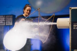 Eine Mitarbeiterin der DLR-Raumfahrt-Show erzeugt auf der Bühne der Lausitzhalle Hoyerswerda mit einer Luftströmung und Nebel eine große schwebende Seifenblase. Das Experiment demonstriert physikalische Effekte und Luftbewegungen.