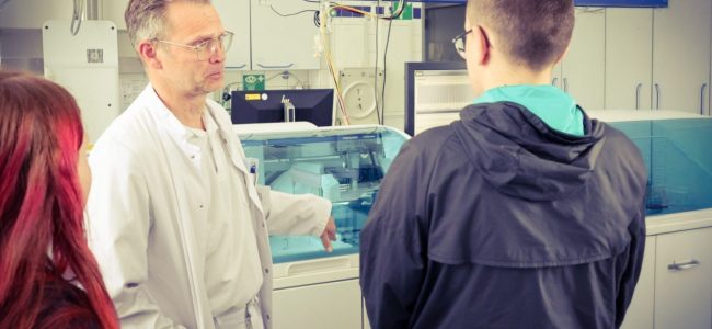 Ein Mitarbeiter des Lausitzer Seenland Klinikums erklärt zwei Jugendlichen in einem Laborbereich medizinische Geräte und Arbeitsabläufe während einer Praxistour im Rahmen des Zukunftsfeldes Gesundheit.