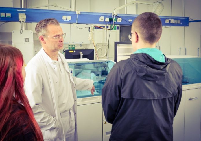 Ein Mitarbeiter des Lausitzer Seenland Klinikums erklärt zwei Jugendlichen in einem Laborbereich medizinische Geräte und Arbeitsabläufe während einer Praxistour im Rahmen des Zukunftsfeldes Gesundheit.
