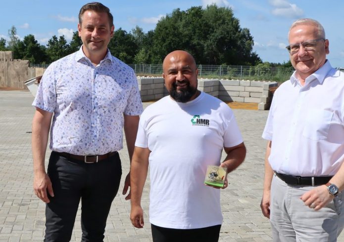 Drei Männer stehen auf dem Betriebsgelände der Hoyerswerda Metall Recycling GmbH im Gewerbegebiet Nardt. Von links nach rechts: Christian Hoffmann, Geschäftsführer Hajrudin Hidanovic und Oberbürgermeister Torsten Ruban-Zeh. Hajrudin Hidanovic hält ein kleines Präsent in den Händen. Im Hintergrund sind die befestigten Betriebsflächen des neu eröffneten Recyclingunternehmens zu sehen.