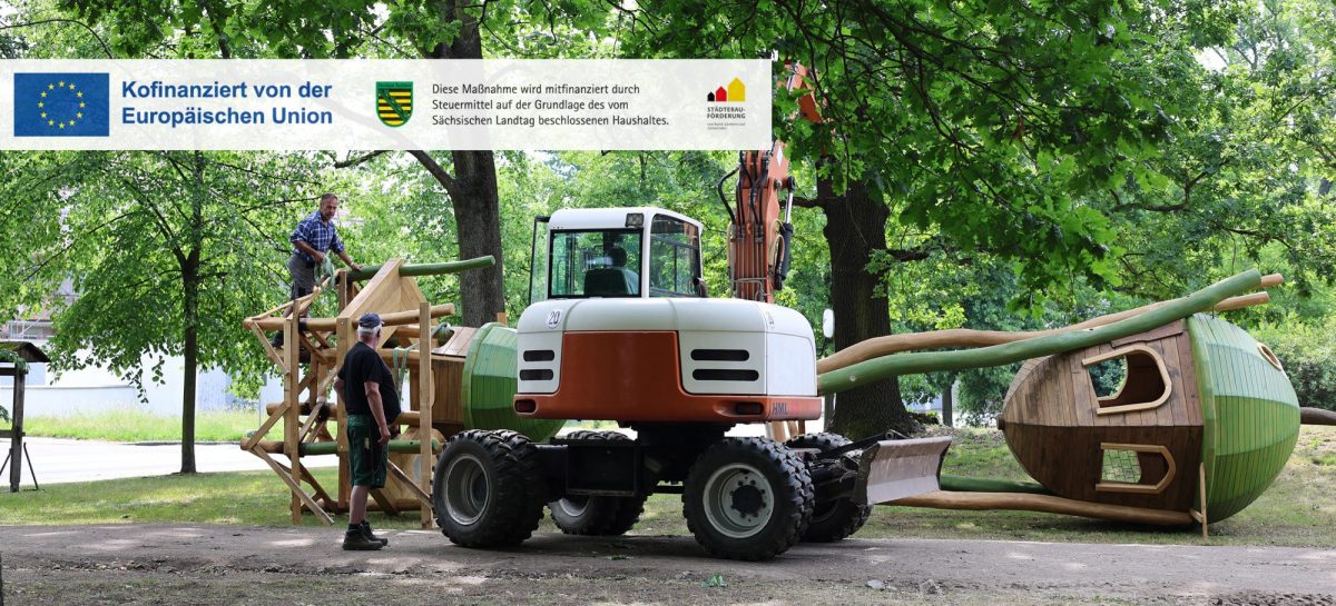 Mitarbeiter montieren mit Unterstützung eines Baggers ein großes Holzspielgerät auf dem Gelände des neuen Spielplatzes im Altstadtpark.