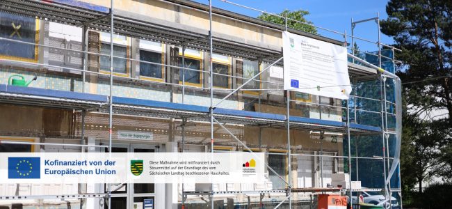 Zweigeschossiges Gebäude mit der Aufschrift „Haus der Begegnungen" vollständig eingerüstet. An der Fassade sind teilweise bereits Dämmplatten angebracht. Ein Bauschild der Stadt Hoyerswerda mit EU-Förderlogo ist am Gerüst befestigt.