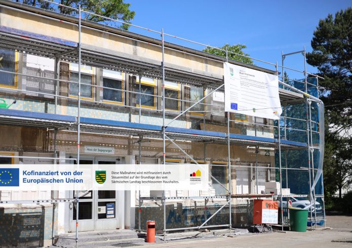 Zweigeschossiges Gebäude mit der Aufschrift „Haus der Begegnungen" vollständig eingerüstet. An der Fassade sind teilweise bereits Dämmplatten angebracht. Ein Bauschild der Stadt Hoyerswerda mit EU-Förderlogo ist am Gerüst befestigt.