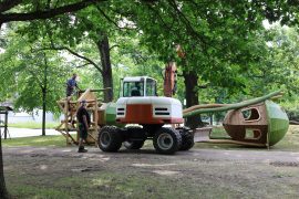 Mitarbeiter montieren mit Unterstützung eines Baggers ein großes Holzspielgerät auf dem Gelände des neuen Spielplatzes im Altstadtpark.