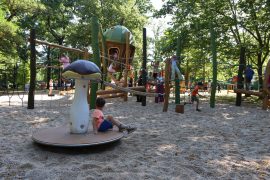 Kinder spielen auf den Kletterelementen des neuen Spielplatzes, im Vordergrund sitzt ein Junge auf einem drehbaren Pilz-Spielgerät.