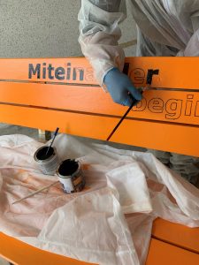 Projektfortschritt: Die Bänke sind Orange und nun geht es ans Aufbringen der Botschaften. Eine davon erhält das Zitat: "Miteinander beginnt, wo Gewalt endet."