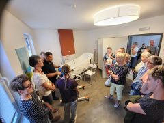 Eine Gruppe von Besucherinnen und Besuchern steht in einem hellen Pflegeraum. Ein Mitarbeiter erläutert die Ausstattung des Raumes. Im Mittelpunkt steht eine große weiße Pflege- beziehungsweise Badewanne mit verschiedenen Halte- und Sitzhilfen.