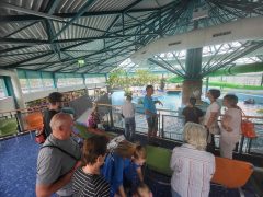 Eine Gruppe von Besucherinnen und Besuchern steht auf einer Empore im Innenbereich des Lausitzbades. Im Hintergrund sind ein Schwimmbecken, eine Wasserrutsche und weitere Bereiche des Bades zu sehen.