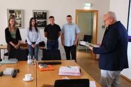 Vier junge Menschen stehen nebeneinander in einem Besprechungsraum. Rechts vor ihnen liest Oberbürgermeister Torsten Ruban-Zeh aus einem Dokument vor.