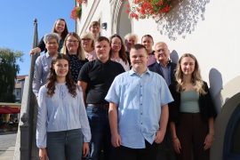 Vier junge Menschen stehen vor einer größeren Gruppe aus Oberbürgermeister Torsten Ruban-Zeh und mehreren Ausbilderinnen auf der Treppe vor dem Rathaus. Alle blicken in die Kamera.