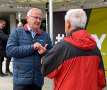Oberbürgermeister Torsten Ruban-Zeh steht unter einem Pavillon mit #WHY!-Beschriftung und spricht mit einem Mann in rot-schwarzer Jacke, der mit dem Rücken zur Kamera steht.
