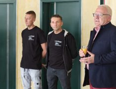 Zwei Mitarbeiter der Seenland Autowerkstatt stehen gemeinsam mit Oberbürgermeister Torsten Ruban-Zeh im Innenbereich des Betriebs. Die Mitarbeiter tragen schwarze T-Shirts mit dem Firmenlogo.