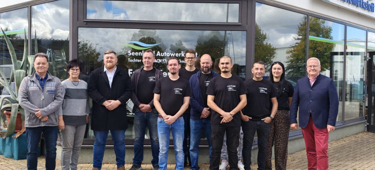 Eine Gruppe von elf Personen steht vor dem Gebäude der Seenland Autowerkstatt.