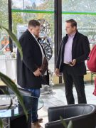 Zwei Männer stehen im Innenbereich der Seenland Autowerkstatt im Gespräch. Im Hintergrund sind mehrere ausgestellte Autofelgen und die große Fensterfront des Betriebes zu sehen.
