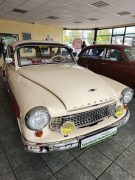 Ein cremefarbener historischer Wartburg mit Chromdetails steht im Innenbereich der Seenland Autowerkstatt. Im Hintergrund ist ein weiteres historisches Fahrzeug zu sehen.