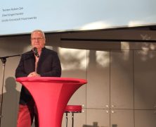 Oberbürgermeister Torsten Ruban-Zeh steht an einem roten Stehtisch mit Mikrofon und begrüßt die Gäste des Unternehmerabends. Hinter ihm ist die Veranstaltungspräsentation „Wirtschaft. Wandel. Wir.“ zu sehen.
