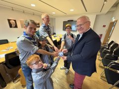 Oberbürgermeister Torsten Ruban-Zeh hält gemeinsam mit mehreren Pfadfindern einen Aufkleber mit dem Pfadfinderzeichen in den Händen. Die Gruppe steht in einem Besprechungsraum des Rathauses.