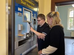Hagen Schill steht gemeinsam mit einer Mitarbeiterin des Bürgerservice vor dem Kassenautomaten der Stadt Hoyerswerda und lässt sich dessen Bedienung erklären.
