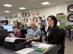 Beate Gröger sitzt gemeinsam mit Bianka Lyssy und Thomas Kloß am Arbeitsplatz im ServiceCenter der Lausitzer Werkstätten. Im Hintergrund sind Fahrräder und Fahrradteile zu sehen.