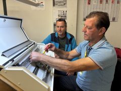 Matthias Kummer sitzt neben einem Mitarbeiter an einem geöffneten Schaltschrank und arbeitet mit einem Schraubendreher an den elektrischen Bauteilen.