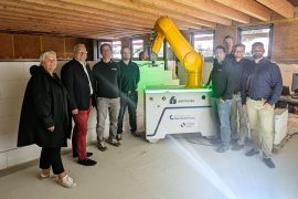 Kathrin Schlesinger, Geschäftsführerin Lautech GmbH, Oberbürgermeister Torsten Ruban-Zeh und eine Gruppe von Projektbeteiligten stehen in einem Baustellenraum rund um den gelben WallBot. Hinter dem Baurobotiksystem ist bereits errichtetes Mauerwerk zu sehen.
