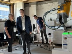 Bürgermeister Mirko Pink steht mit Lautech-Geschäftsführerin Kathrin Schlesinger vor dem gelben Baurobotiksystem WallBot. Im Hintergrund ein Mitarbeiter mit Blick auf die Technik.