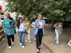Mehrere Frauen und Mädchen gehen gemeinsam über das Außengelände einer Einrichtung. Eine Frau im hellblauen Blazer führt die Gruppe und spricht dabei zu den Teilnehmenden.