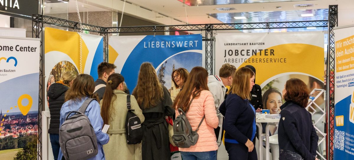 Mehrere Besucherinnen und Besucher stehen vor den Messeständen des Landratsamtes Bautzen und des Jobcenters und sprechen mit den Ausstellenden.