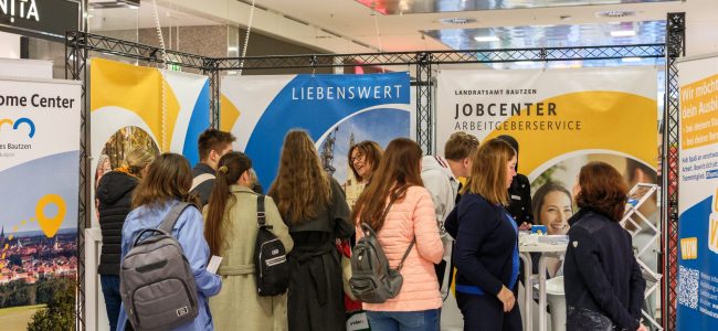 Mehrere Besucherinnen und Besucher stehen vor den Messeständen des Landratsamtes Bautzen und des Jobcenters und sprechen mit den Ausstellenden.