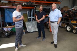 Tommy Schimang spricht in einer Lager- und Werkstatthalle mit Wirtschaftsförderer Sebastian Schindler und Oberbürgermeister Torsten Ruban-Zeh. Im Hintergrund stehen Regale mit Geräten, Werkzeugen und Maschinen.