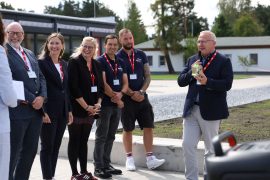 Oberbürgermeister Torsten Ruban-Zeh spricht vor mehreren Gästen und Beschäftigten der DB Bahnbau Gruppe. In seinen Händen hält er den als Geschenk verpackten Krabat-Raben.