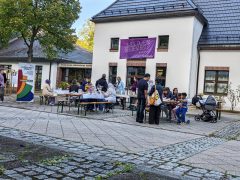 Erwachsene und Kinder sitzen und stehen an gedeckten Tischen vor dem Martin-Luther-King-Haus. Links stehen Ausstellungstafeln und ein Banner der Initiative Zivilcourage.