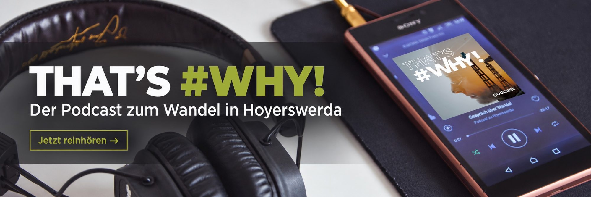 Breiter Banner mit schwarzen Kopfhörern links und einem Smartphone rechts, auf dem das Podcastcover zu sehen ist. Im Vordergrund steht: „THAT’S #WHY! Der Podcast zum Wandel in Hoyerswerda. Jetzt reinhören“.