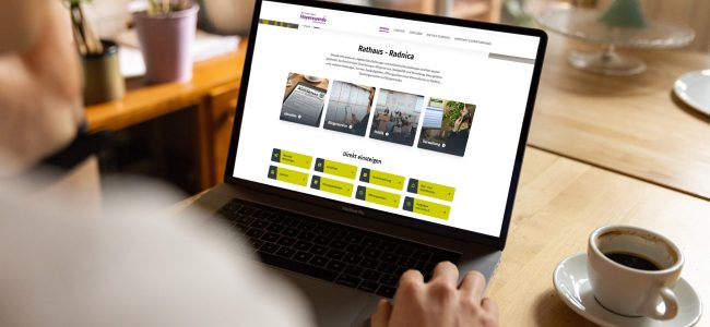 Bildmontage: Eine Person sitzt an einem Holztisch vor einem Laptop. Auf dem Bildschirm ist der Bereich „Rathaus“ der Website hoyerswerda.de zu sehen. Neben dem Laptop steht eine Kaffeetasse.